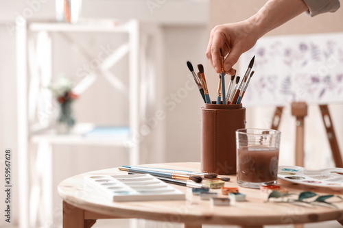 Watercolorist taking brush from holder on table in workshop, closeup