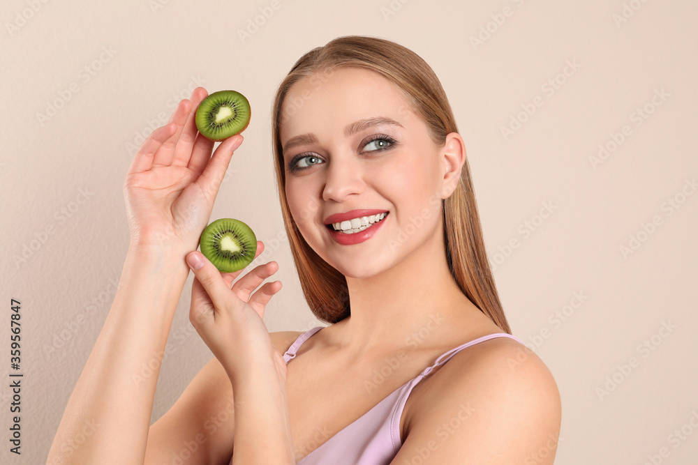 Young woman with cut kiwi on beige background. Vitamin rich food Young woman with cut kiwi on beige background. Vitamin rich food