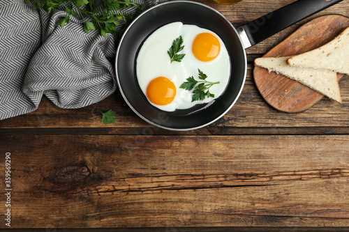 Tasty cooked chicken eggs with parsley in frying pan on wooden table, flat lay. Space for text