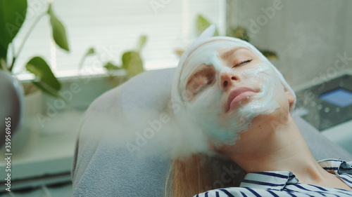 Medium close-up shot of professional facial skin care treatment with a cosmetic steamer at beauty salon. The Steam cleaning procedure of the face.