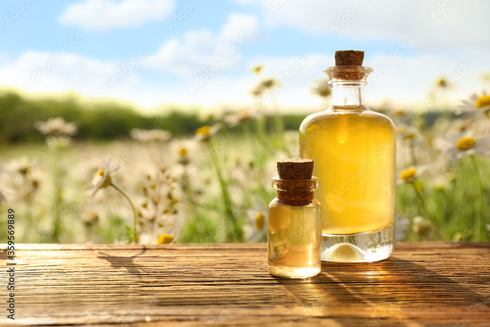 Bottles of chamomile essential oil on wooden table in field. Space for text Bottles of chamomile essential oil on wooden table in field. Space for text