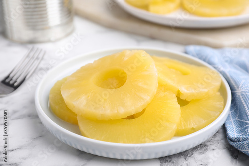 Tasty canned pineapple slices on white marble table, closeup