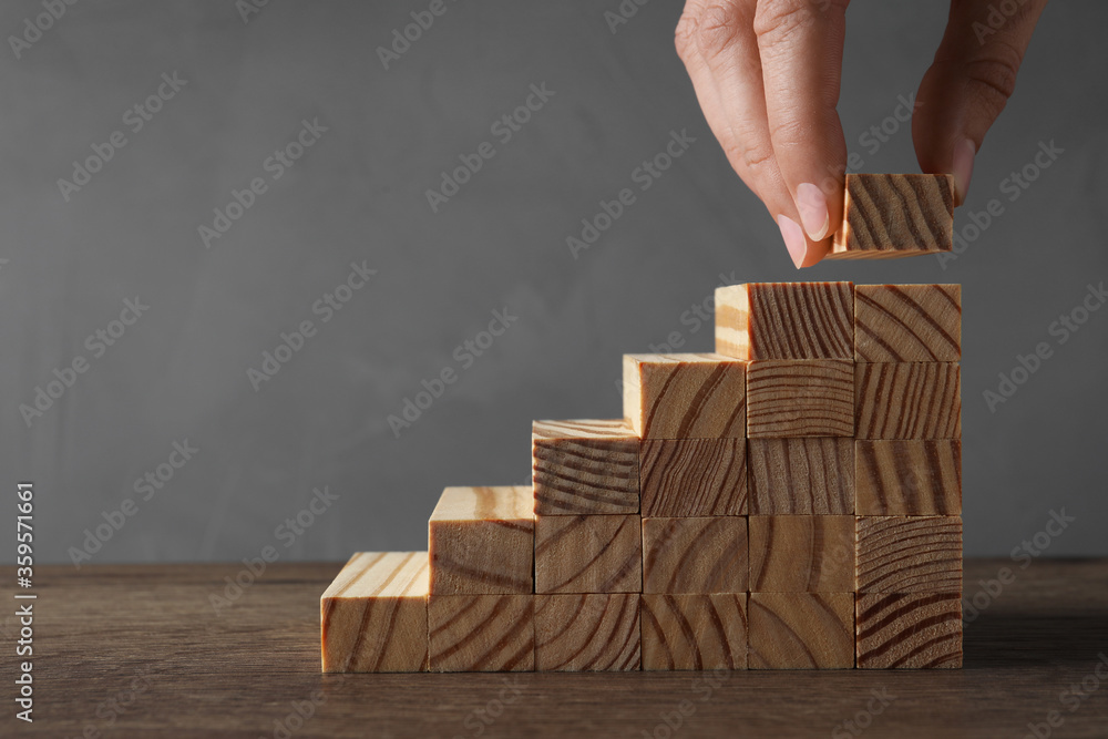Closeup view of woman building steps with wooden blocks at table, space for text. Career ladder