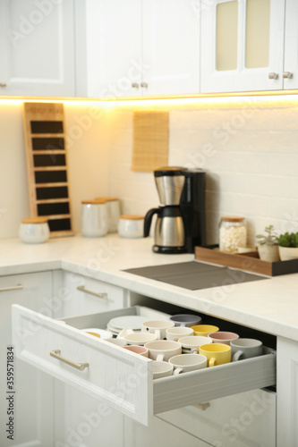 Open drawer with cups and coffeemaker on countertop in kitchen © New Africa