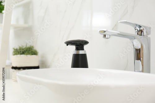Modern automatic soap dispenser near sink in bathroom  closeup