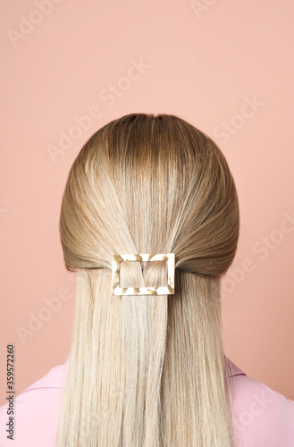 Young woman with beautiful gold hair clip pin on pink background, back view photo
