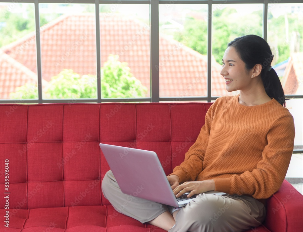 Asia woman is smiling with working to laptop and sitting on red sofa at her room Asia woman is smiling with working to laptop and sitting on red sofa at her room