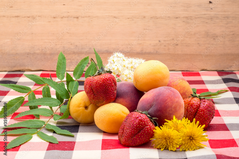 Strawberries, peach, apricot, rowan flower, yellow dandelion lie on the table on the tablecloth