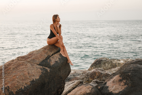 Beautiful blonde woman sitting on a rock by the sea. The style of summer holiday. Modern girl