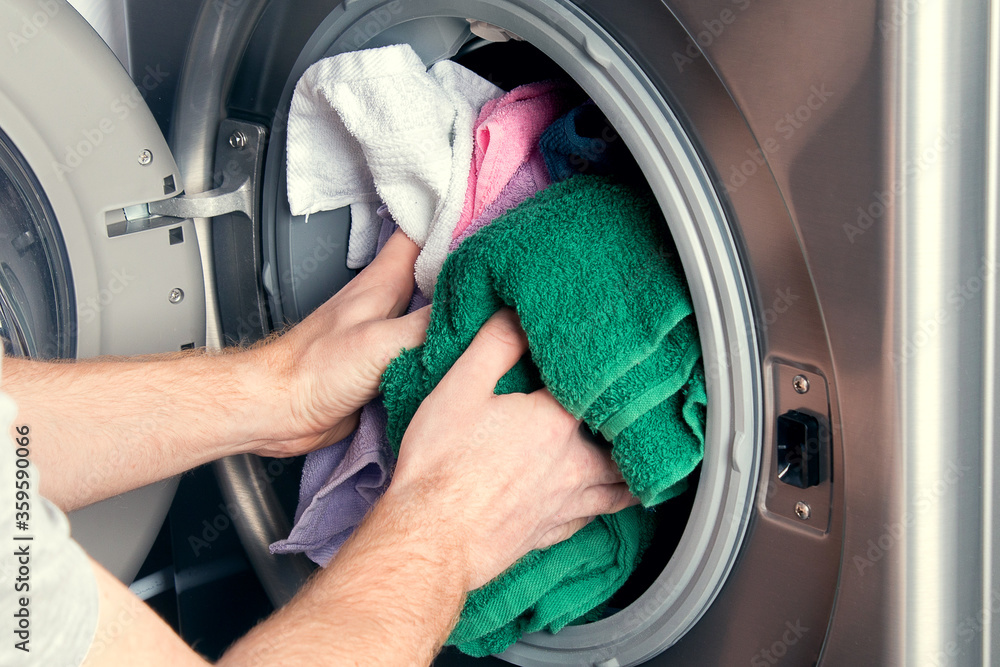 Man taking color clothes from washing machine. A drum of washing machine full of dirty laundry in the bathroom. Man taking color clothes from washing machine. A drum of washing machine full of dirty laundry in the bathroom.