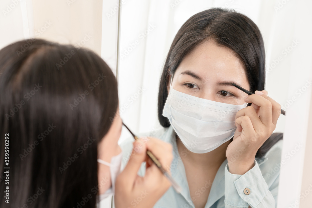 Mirror reflection asian woman wear surgical face mask apply cosmetic make up for go out to work after unlock Coronavirus lockdown. Reopenning , restart, Self-quarantine and social distancing concept.