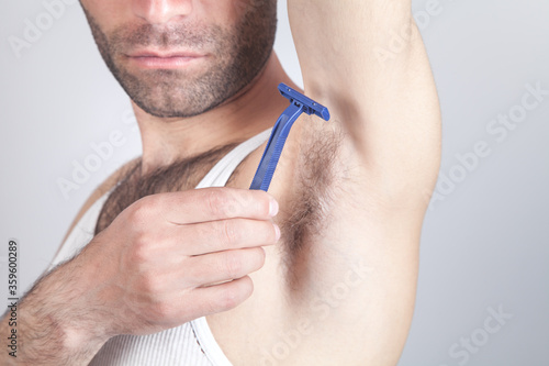 Caucasian man with disposable razor shaving his armpit.