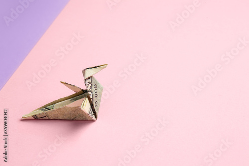 Origami bird made of dollar banknote on color background