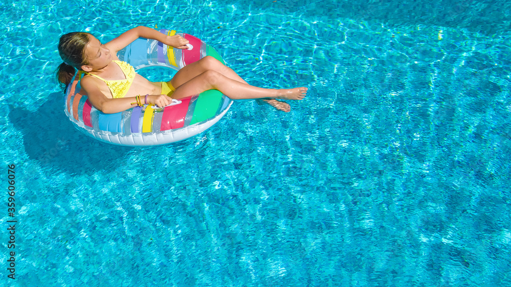 Acrive girl in swimming pool aerial top view from above, kid swims on inflatable ring donut , child has fun in blue water on family vacation resort
