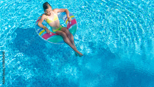Acrive girl in swimming pool aerial top view from above, kid swims on inflatable ring donut , child has fun in blue water on family vacation resort 