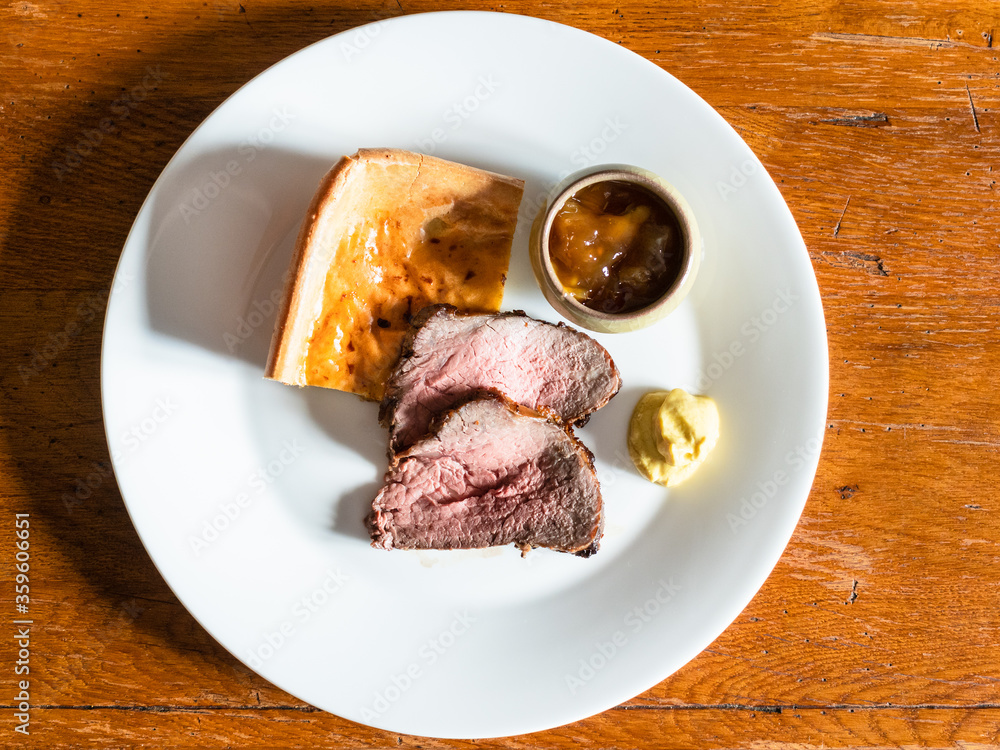top view of served home-made sliced Roast Beef and piece of Yorkshire pudding with mustard and sauce on white plate on old wooden table at home kitchen top view of served home-made sliced Roast Beef and piece of Yorkshire pudding with mustard and sauce on white plate on old wooden table at home kitchen