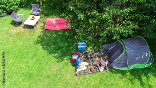 Aerial top view of campsite from above, mother and daughter having fun, tent and camping equipment under tree, family vacation in camp outdoors concept 