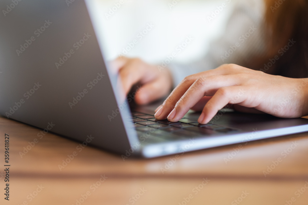 Closeup image of a woman working and typing on laptop computer keyboard on wooden table Closeup image of a woman working and typing on laptop computer keyboard on wooden table