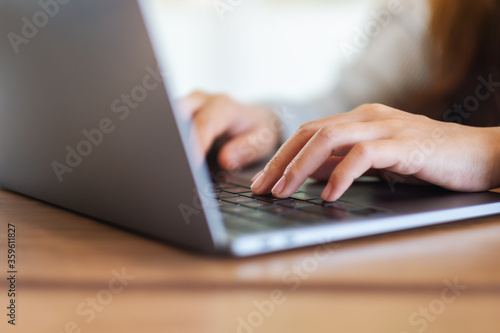 Closeup image of a woman working and typing on laptop computer keyboard on wooden table