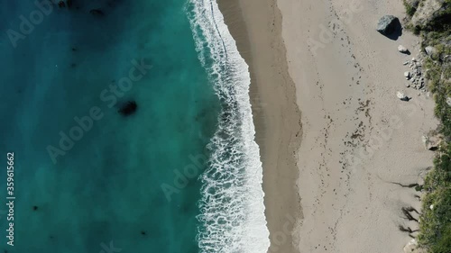 Aerial top down shot of turquoise ocean and waves washing up on Big Sur beach