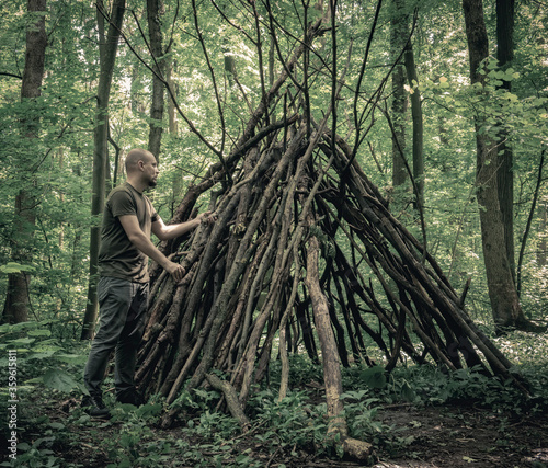 Man building a survival shelter in the forest. Shelter in the woods from tree branches. photo