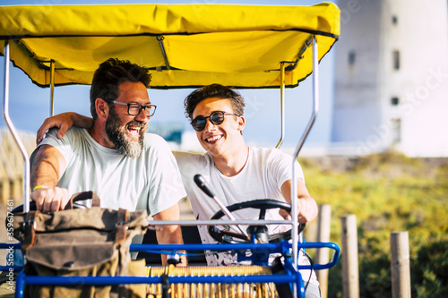 Father and son family together on a surrey bike have fun in outdoor leisure activity or summer holiday vacation - cheerful people laugh and smile with different ages and generations