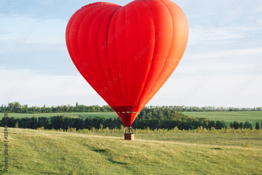 Fototapeta premium Hot air balloon in shape of heart is landing on the green field