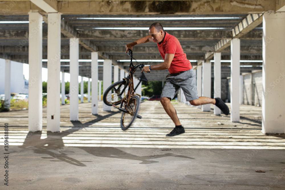 Man in color t-shirt on the bike. Bmx rider performing tricks at street with striped shadow from the sun Man in color t-shirt on the bike. Bmx rider performing tricks at street with striped shadow from the sun