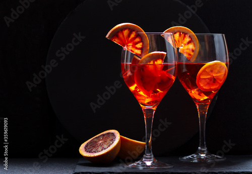 Two glasses of aperol spritz drink with blood orange slices on dark background