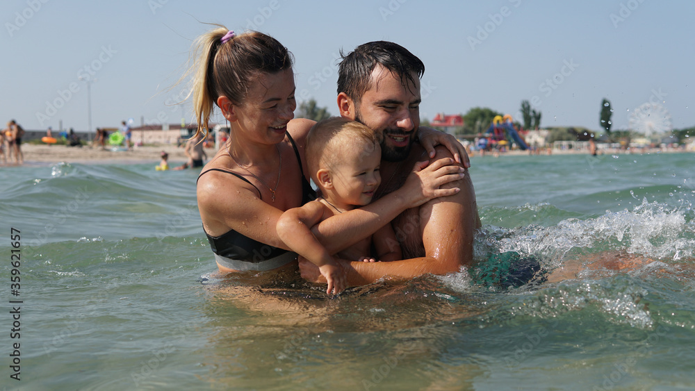Young family hugging in water in sea. Father holding little son in arms Young family hugging in water in sea. Father holding little son in arms