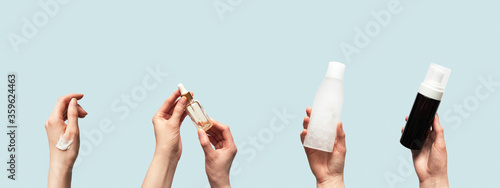 Hands up holding beauty cosmetic products isolated on blue background horizontal banner format. Woman takes oil serum, toner or tonic bottle, facial foam cleanser and smear smudge moisturizer cream photo