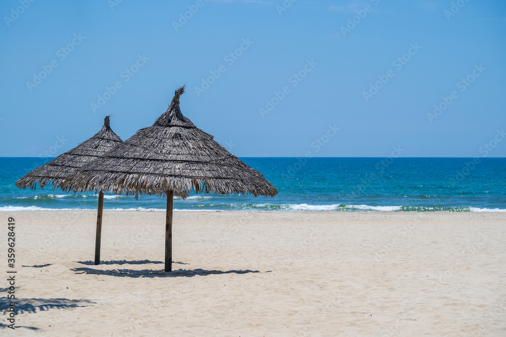 Tropical sand beach and summer sea water with blue sky and two straw umbrella. Travel and nature concept Tropical sand beach and summer sea water with blue sky and two straw umbrella. Travel and nature concept