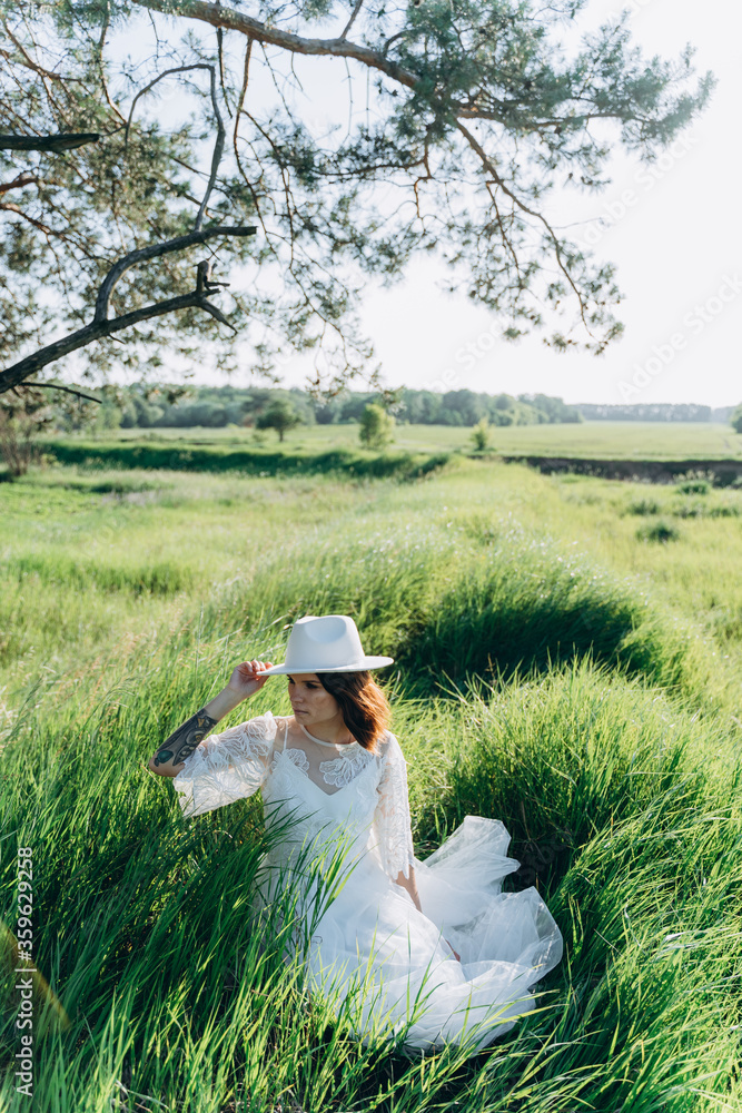 stylish woman holding fedora hat in hands and sitting in summer field stylish woman holding fedora hat in hands and sitting in summer field