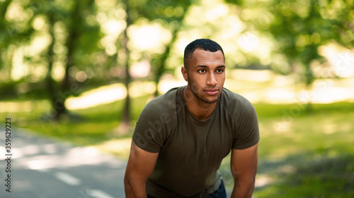 Millennial black guy on jogging track at park, resting after his morning workout