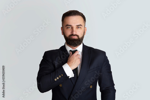 Successful businessman in office wear touching his necktie on grey background