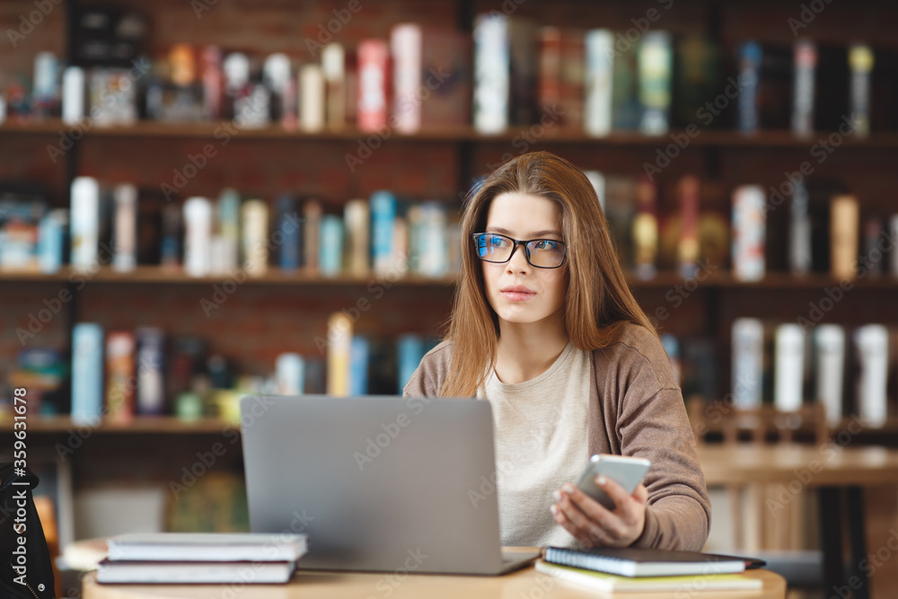 Thoughtful Brunette girl using laptop and smartphone and looking aside Thoughtful Brunette girl using laptop and smartphone and looking aside