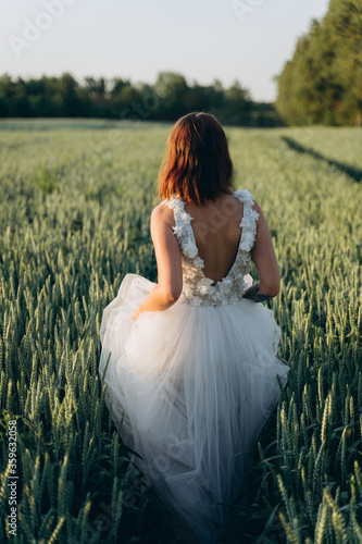 back view of attractive young woman in long white dress standing in the field 