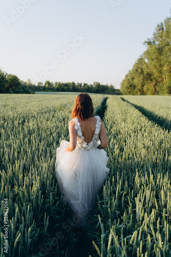 back view of attractive young woman in long white dress standing in the field 