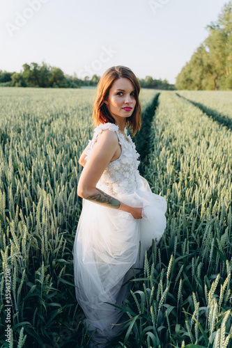 attractive young woman in long white dress standing in the field and looking at camera