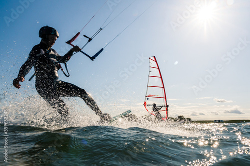 Kitesurfer and windsurfer having fun on the water while backlit from the sun photo