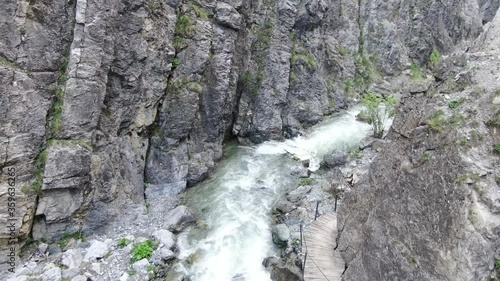 Aerial shot of a stormy river in a gorge / canyon with a wooden path turning around the rocks photo