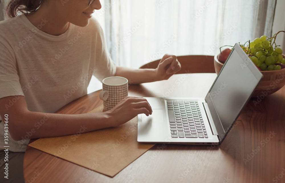 Fototapeta premium Woman sitting at the kitchen table and connecting with her laptop