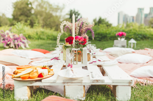 Festive summer picnic with tasty snacks, fruits and wine, decorated with beautiful flowers and candles in pink colors for hen-party. Good food serving. Event agency. Selective focus