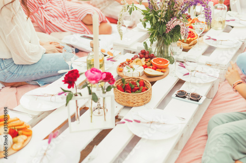 Group of young women enjoying a summer picnic with tasty snacks, cheese, fruits, strawberry berries, white wine and cold lemonade. Food and drink concept. Friendship and fun, Flowers decoration
