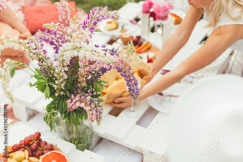Summer garden picnic. Young blonde woman set the table for birthday celebration or hen-party. Flowers decoration. Friendship, leisure and fun. Pleasure time for friends © Kate