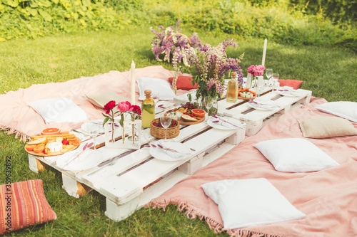 Beautiful summer celebration picnic in the garden with tasty food and cold drinks. Pallet table, Flowers decoration. Pleasure time with friends. Leisure and fun