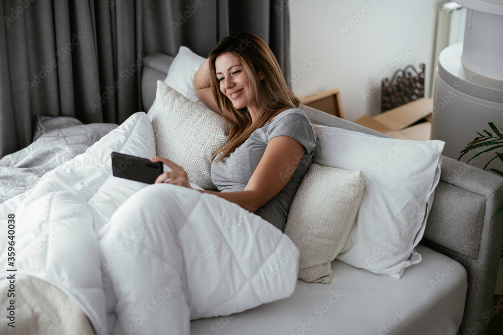 Young beautiful woman using phone in bed. Girl lying on bed. Young beautiful woman using phone in bed. Girl lying on bed.