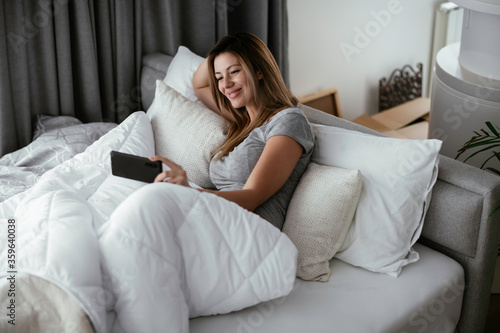 Young beautiful woman using phone in bed. Girl lying on bed. 
