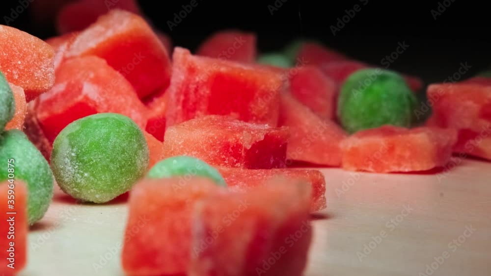 Sliced frozen vegetables spill out onto a wooden table. closeup frozen green peas and orange carrots. Sliced frozen vegetables spill out onto a wooden table. closeup frozen green peas and orange carrots.