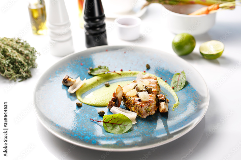 Grilled tuna steak with pistachio nuts, capers and green peas. Tasty dish on a blue plate. Food photography.